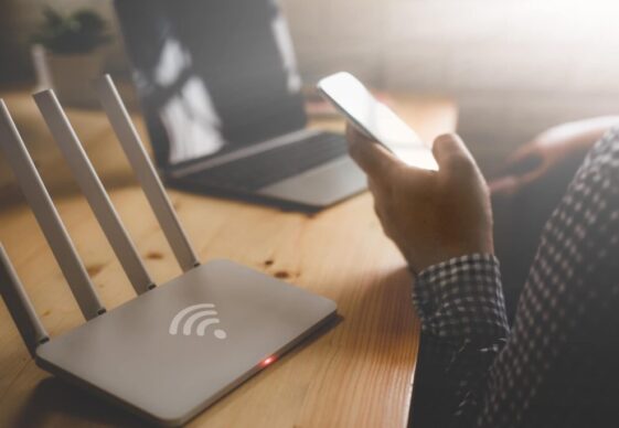 Primer plano de un enrutador inalámbrico y un hombre usando un teléfono inteligente en la sala de estar de una oficina en casa.